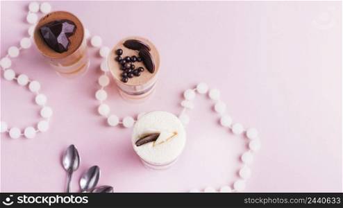 overhead view layered desserts with decoration pink backdrop with necklace spoons