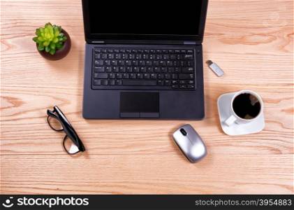 Overhead view of a clean desk consisting of laptop, baby plant, mouse, thumb drive, coffee, and reading glasses.