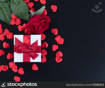 Overhead view of a gift box, heart shapes and a single red rose on dark stone background