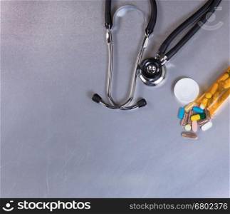Overhead view of a medical stethoscope and pills on stainless steel table