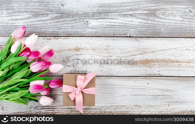 overhead view of a springtime pink tulips and brown gift box on white weathered wooden boards