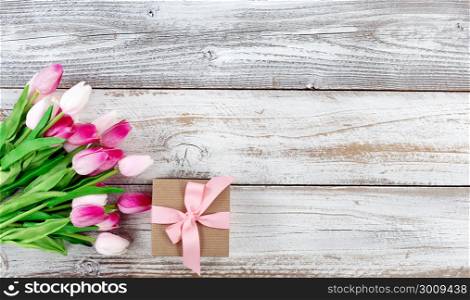 overhead view of a springtime pink tulips and brown gift box on white weathered wooden boards