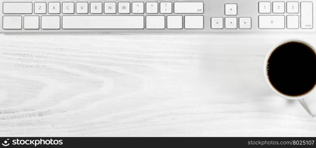 Overhead view of a white desktop with keyboard and coffee.
