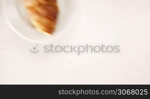 Overhead view of a woman enjoying a cup of black espresso coffee and a freshly baked croissant for breakfast. High angle close up.