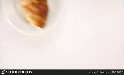 Overhead view of a woman enjoying a cup of black espresso coffee and a freshly baked croissant for breakfast. High angle close up.