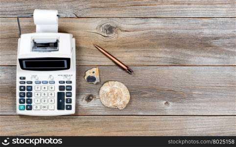 Overhead view of an adding machine and paper roll on stressed wood with stone fossils. Obsolete technology concept.