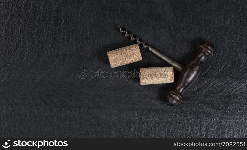 Overhead view of antique wine corkscrew and used corks on black slate