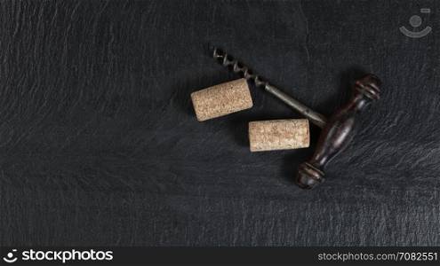 Overhead view of antique wine corkscrew and used corks on black slate
