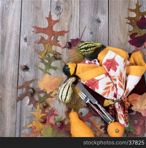 Overhead view of autumn dinner setting with real gourd decorations, leaves and acorns on top of rustic wood