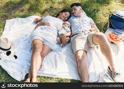 Overhead view of baby boy lying between parents on picnic blanket in Pelham Bay Park, Bronx, New York, USA