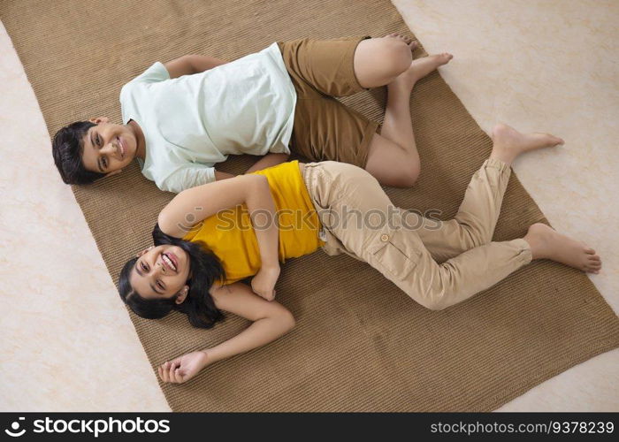 Overhead view of cheerful boy and girl lying down on floor in living room