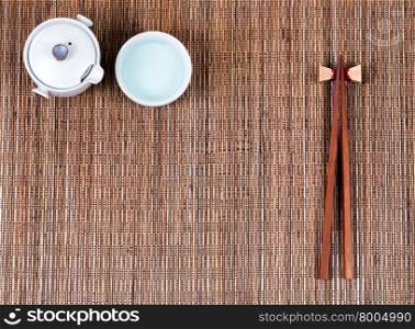 Overhead view of chopsticks, cup and tea server on bamboo mat.