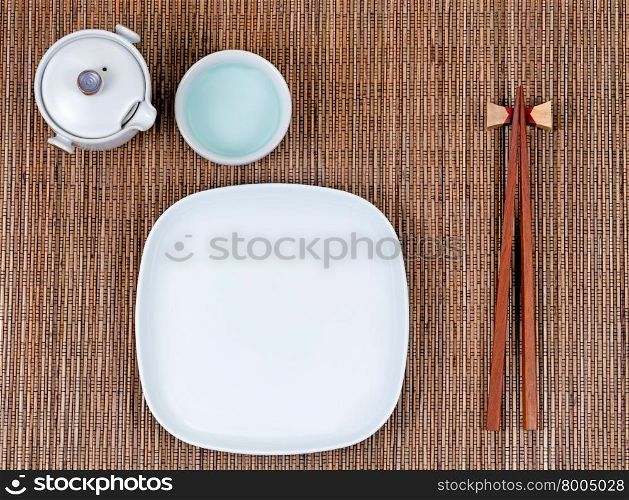 Overhead view of chopsticks, plate, cup and tea server on bamboo mat.