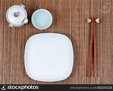 Overhead view of chopsticks, plate, cup and tea server on bamboo mat.