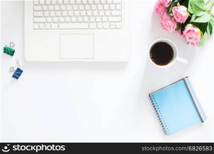 Overhead view of computer laptop, a cup of coffee, pink roses and notebook on white background, Copy space