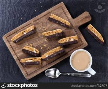 Overhead view of cookies with dark chocolate and nuts on wooden server board with coffee on dark stone background