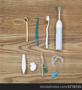 Overhead view of dental maintenance tools placed on aged wooden boards. Items include hand tooth brush, picks, whitening trays, gel, mirror, floss, toothpaste tube, and electric tooth brush.
