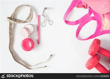 Overhead view of essential beauty items, red dumbbells, sport bra and cosmetic, top view isolated on white background