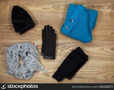 Overhead view of fall or winter clothing and accessories placed on rustic wooden boards. Items include gloves, hat, wool socks, scarf, and sweater.
