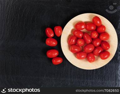 Overhead view of fresh cherry tomatoes on bamboo plate with black slate