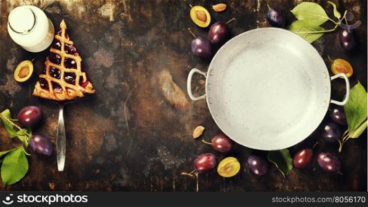 overhead view of fresh plum pie or tart and plums on dark rustic background
