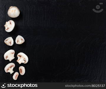 Overhead view of fresh whole and sliced mushrooms, left side of frame, on black slate.