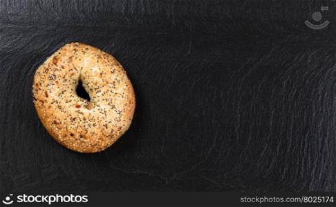 Overhead view of freshly baked seeded bagel on natural slate stone.