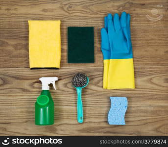 Overhead view of house cleaning materials placed on rustic wood. Items include sponge, rubber gloves, stainless steel pad, spray bottle, microfiber rag, and scrub pad.