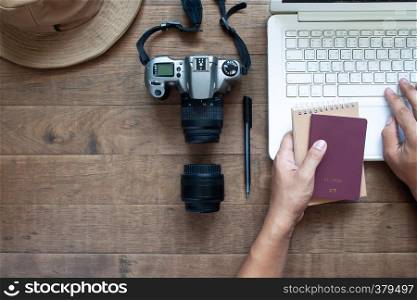 Overhead view of man hands using laptop and holding passport and camera on wooden background