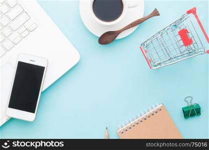 Overhead view of modern work space with laptop, mobile device and cup of coffee with shopping cart, Online and business marketing on pastel color background