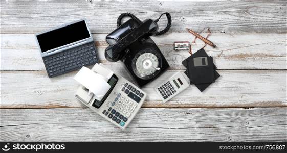 Overhead view of obsolete technologies that includes rotary dial phone and old computer data storage devices plus calculators