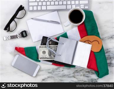 Overhead view of office desktop with computer keyboard, cell phone, shopping bag, wallet, money, pen, paper, reading glasses, coffee and Xmas Stocking on marble surface. Shopping for Christmas concept.