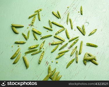 Overhead view of peas in pea pods on green background