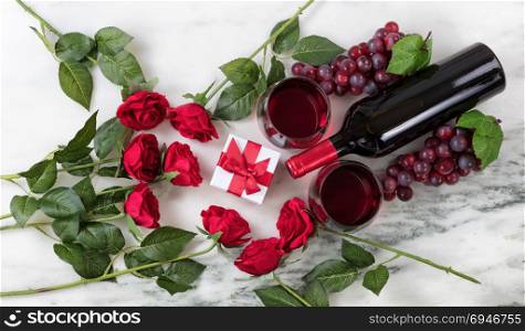 Overhead view of Red wine bottle, glasses, grapes and roses on natural marble stone setting