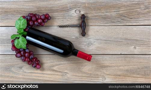Overhead view of Red wine bottle with grapes and corkscrew on weathered wooden boards
