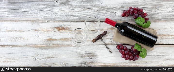 Overhead view of Red wine bottle with grapes, empty drinking glasses and corkscrew on weathered wooden boards