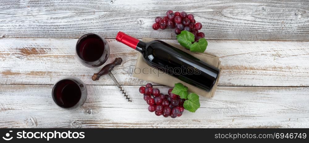 Overhead view of Red wine bottle with grapes, filled drinking glasses and corkscrew on weathered wooden boards