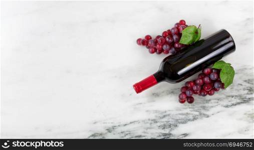 Overhead view of Red wine bottle with grapes on natural marble stone setting