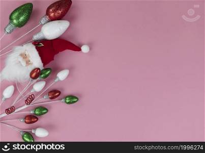 Overhead view of Santa Claus decoration and colorful bulbs on a light pink setting for a Merry Christmas or Happy New Year background