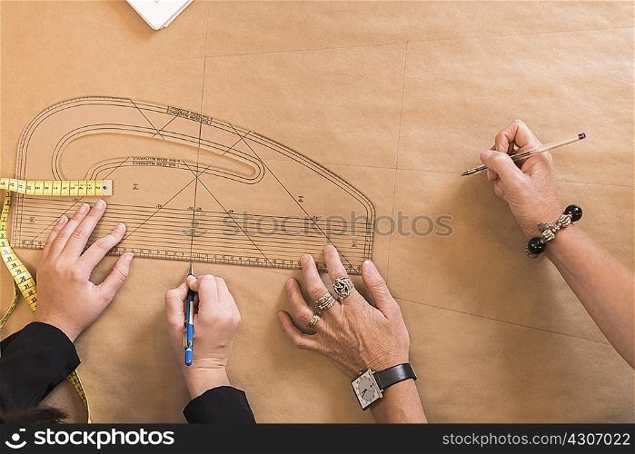 Overhead view of seamstresses hands drawing with curved ruler on dressmakers pattern in workshop