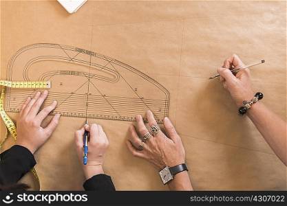 Overhead view of seamstresses hands drawing with curved ruler on dressmakers pattern in workshop