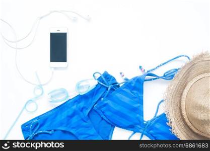 Overhead view of smartphone with bikini, goggles in blue color and summer items on white background