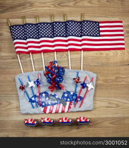 Overhead view of United States of America flags, ribbons, t-shirt, fire cracker, dog tag and pinwheels positioned on rustic wooden boards.