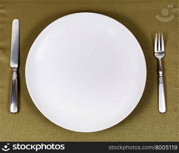 Overhead view of white dinner plate with fork and knife on green table cloth.
