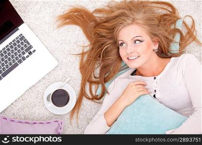 Overhead view of young woman lying on back on carpet alongside laptop, coffee, daydreaming
