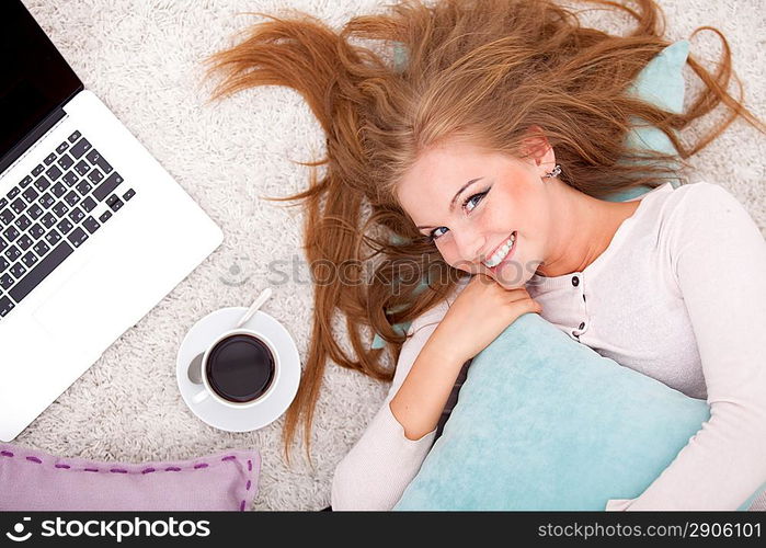 Overhead view of young woman lying on back on carpet alongside laptop, coffee, daydreaming