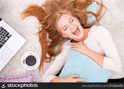 Overhead view of young woman lying on back on carpet alongside laptop, coffee, daydreaming