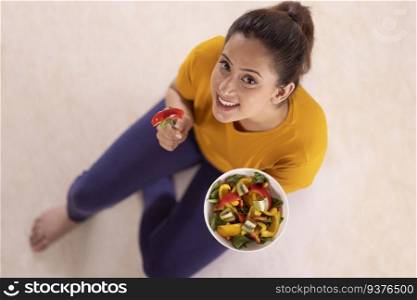 Overhead view of young woman sitting on floor with a salad bowl