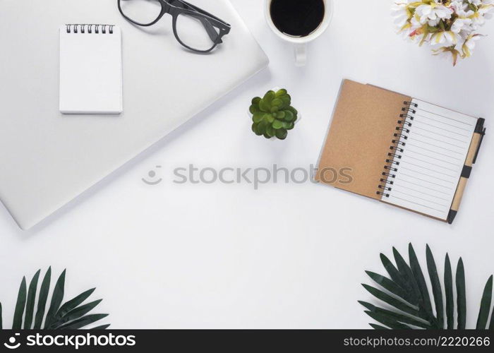 overhead view office stationery with laptop coffee cup flower vase leaves white backdrop