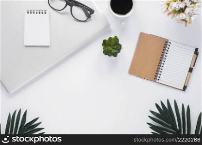 overhead view office stationery with laptop coffee cup flower vase leaves white backdrop